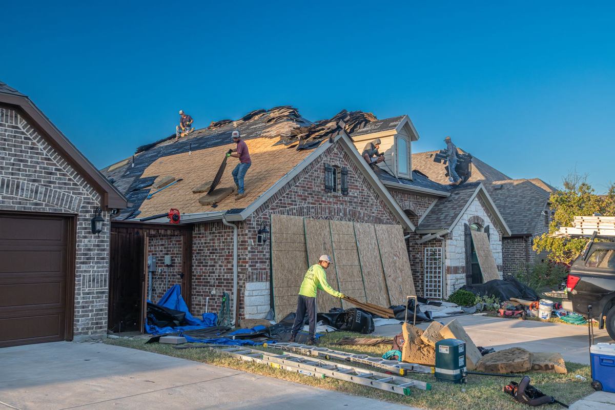 Roof mid tear-off with shingles stripped down to the decking and a work crew on the slope